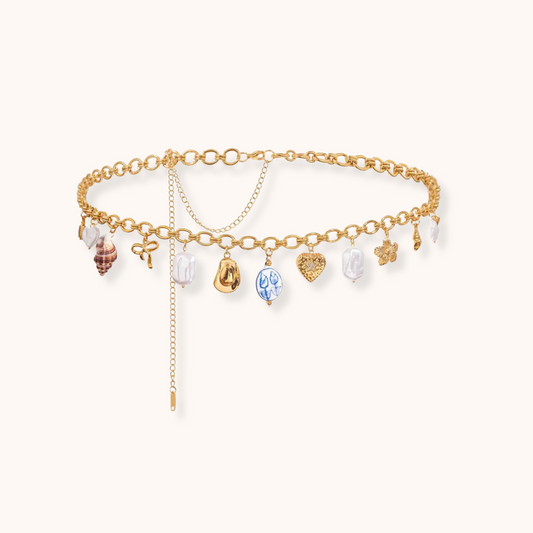 Chunky gold waist chain featuring multiple charms including pearl, shell, heart, and medallion, set on a round-link stainless steel base.